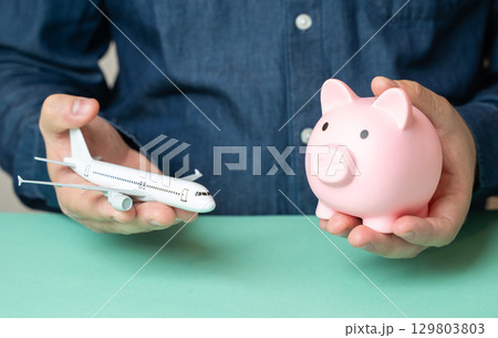 A man holds an airplane and a piggy bank. Travel savings. Budget flights. Cheap tickets. A man holds an airplane and a piggy bank. Travel savings. Budget flights. Cheap tickets. 129803803