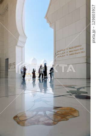 View of Sheikh Zayed Grand Mosque in Abu Dhabi made of white marble with flowers made of precious stones in design and beautiful reflections. Silhouettes of tourists admiring beauty of art. Vertical View of Sheikh Zayed Grand Mosque in Abu Dhabi made of white marble with flowers made of precious stones in design and beautiful reflections. Silhouettes of tourists admiring beauty of art. Vertical 129803917