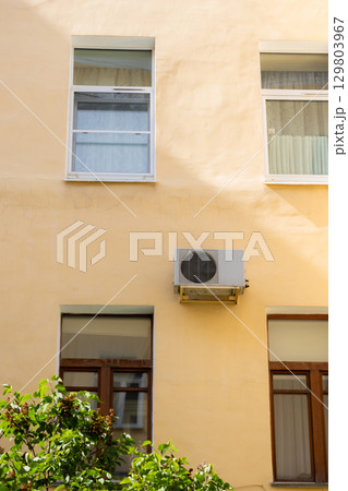 air conditioner on wall of an apartment building with view of green trees. air conditioner on wall of an apartment building with view of green trees. 129803967