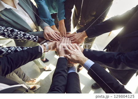 Close up top view photo of diverse business people putting their arms together in stack. Close up top view photo of diverse business people putting their arms together in stack. 129804125