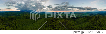 Aerial wide panoramic view of dark mountain hills covered with green mixed pine and lush forest in evening. 129805837