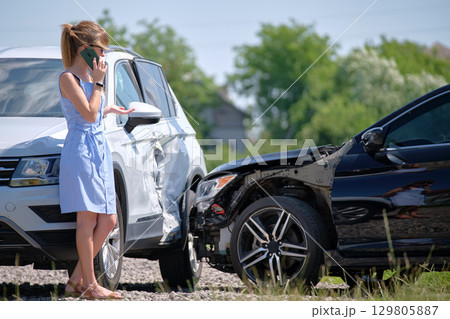 Stressed driver talking on sellphone on roadside near her smashed vehicle calling for emergency service help after car accident. Road safety and insurance concept Stressed driver talking on sellphone on roadside near her smashed vehicle calling for emergency service help after car accident. Road safety and insurance concept 129805887
