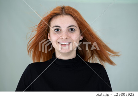 Close up portrait of pretty redhead girl with long wavy hair blowing on the wind. 129805922