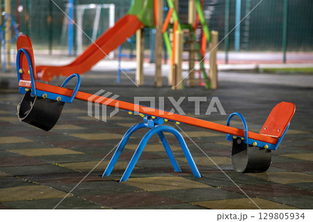 Seesaw swing in preschool yard with soft rubber flooring at night. Seesaw swing in preschool yard with soft rubber flooring at night. 129805934