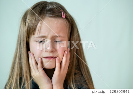 Close-up portrait of unhappy little girl with long hair covering her face with hands crying. 129805941