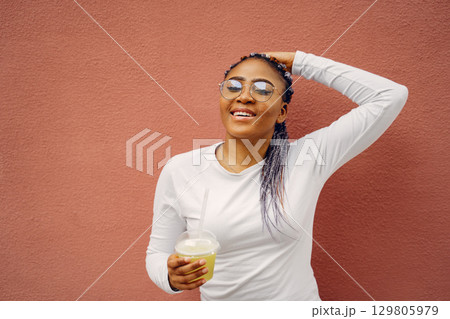 Young black woman with afro hairstyle smiling in a city. Mixed girl with cocktail. 129805979