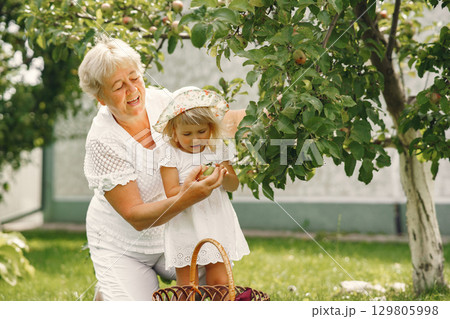 Grandmother and granddaughter together, hugging and joyfully laughing in a Flowering apricot garden in April. Family outdoors lifestyle. Grandmother and granddaughter together, hugging and joyfully laughing in a Flowering apricot garden in April. Family outdoors lifestyle. 129805998