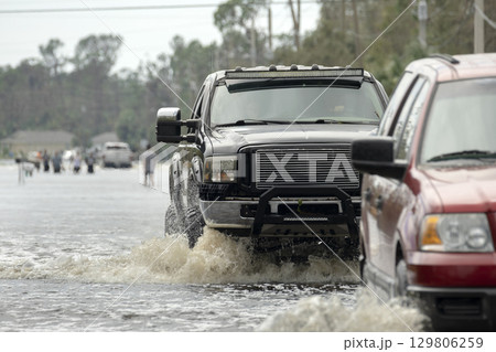 Flooded Florida road with evacuating cars and surrounded with water houses in suburban residential area. Consequences of hurricane natural disaster 129806259
