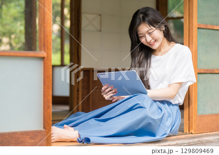 古民家でタブレットを見て笑っている若い女性 古民家でタブレットを見て笑っている若い女性 129809469