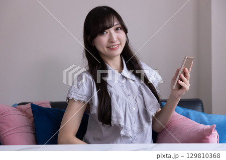 リビングでスマホを持って微笑む日本人女性 リビングでスマホを持って微笑む日本人女性 129810368