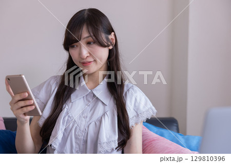 リビングでスマホを持って微笑む日本人女性 リビングでスマホを持って微笑む日本人女性 129810396