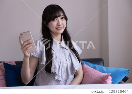 リビングでスマホを持って微笑む日本人女性 リビングでスマホを持って微笑む日本人女性 129810404