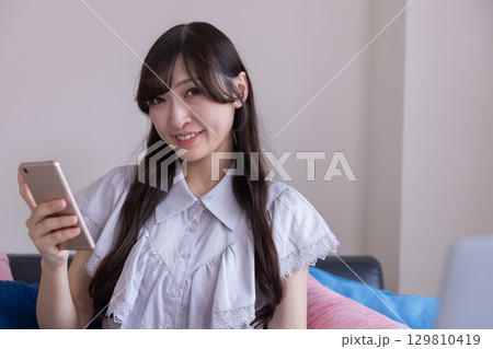 リビングでスマホを持って微笑む日本人女性 リビングでスマホを持って微笑む日本人女性 129810419