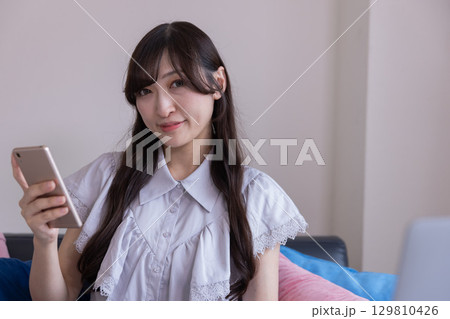 リビングでスマホを持って微笑む日本人女性 129810426