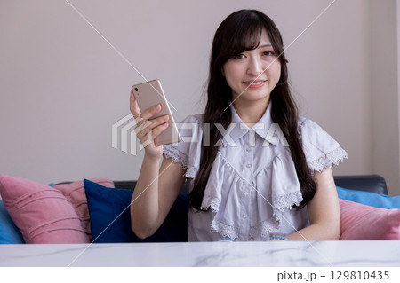 リビングでスマホを持って微笑む日本人女性 リビングでスマホを持って微笑む日本人女性 129810435