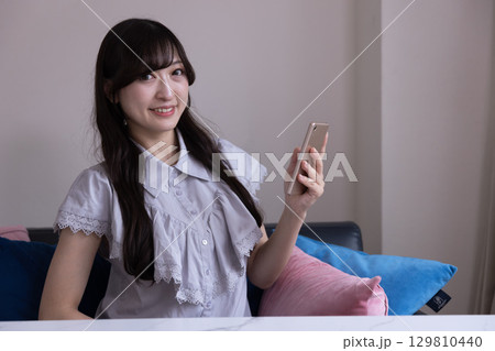 リビングでスマホを持って微笑む日本人女性 129810440