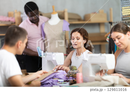 Middle-aged woman talking with man and sewing, other working with mannequin Middle-aged woman talking with man and sewing, other working with mannequin 129811016