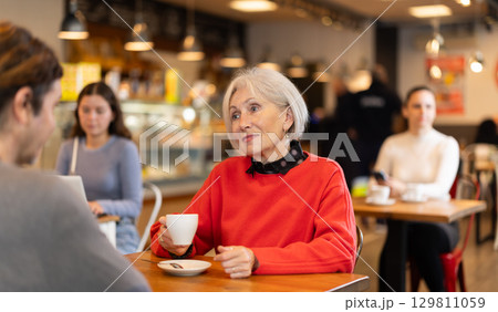 Elderly woman meets a man in a cafe. Conversation over cup of coffee Elderly woman meets a man in a cafe. Conversation over cup of coffee 129811059