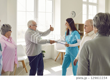 Senior man in retirement home shakes hands with young nurse and gives her thumbs up Senior man in retirement home shakes hands with young nurse and gives her thumbs up 129811154