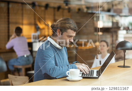 Man using laptop and drinking coffee in modern cafe Man using laptop and drinking coffee in modern cafe 129811167