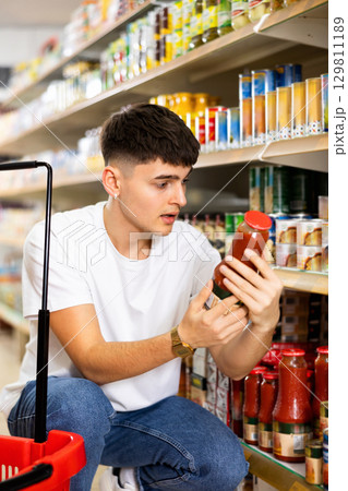 Guy reading label on bottle with tomato juice in supermarket Guy reading label on bottle with tomato juice in supermarket 129811189