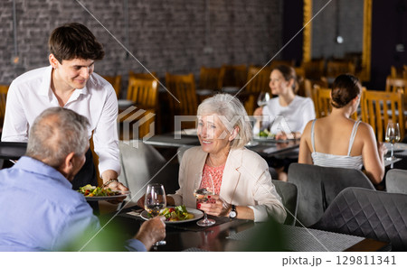 Restaurateur guy serves customers elderly spouses plate with dinner order Restaurateur guy serves customers elderly spouses plate with dinner order 129811341