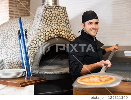 Latino chef in black uniform holding shovel with pizza in kitchen restaurant 129811349