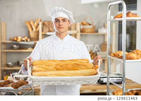 Happy male baker posing with basket of freshly baked baguettes in bakery, demonstrating concept of food industry and baker profession Happy male baker posing with basket of freshly baked baguettes in bakery, demonstrating concept of food industry and baker profession 129811463