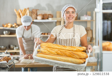 Young woman are standing in kitchen with basket of finished products baguettes 129811538