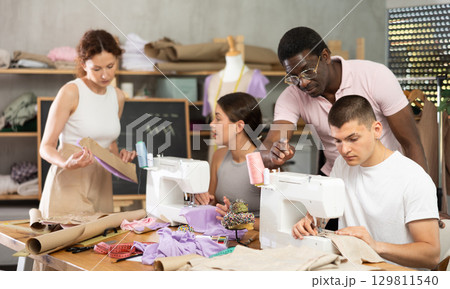 Middle-aged male teacher helping students sew while other works with textile Middle-aged male teacher helping students sew while other works with textile 129811540
