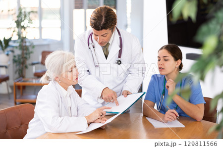 three positive doctors are sitting at table animatedly and actively discussing current work 129811566