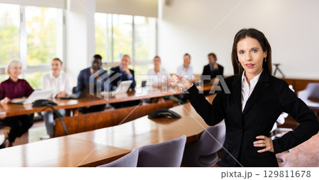 Confident mid-aged white brunette businesswoman posing with presenting hand gesture Confident mid-aged white brunette businesswoman posing with presenting hand gesture 129811678