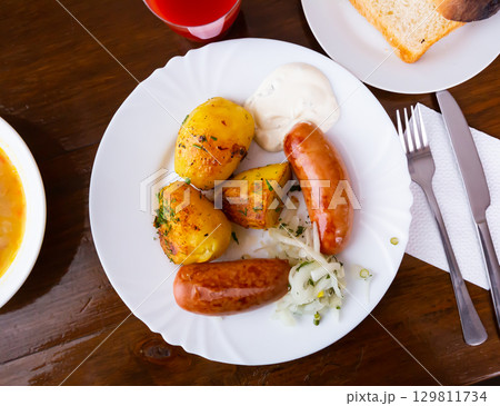 Grilled meat sausages served with potatoes fried with onion 129811734