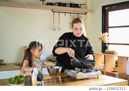 Mother cooking at the stove while her daughter watches attentively 129812311