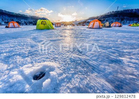 凍った湖の氷上のカラフルなワカサギ釣りのテントと氷点下で寒い早朝の朝日 129812478