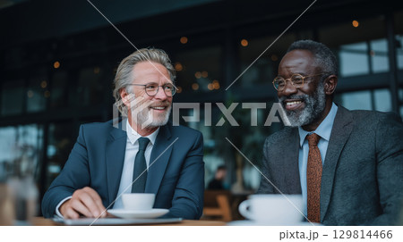 Two senior businessmen in suits smiling and talking over coffee at a cafe or modern business lounge Two senior businessmen in suits smiling and talking over coffee at a cafe or modern business lounge 129814466