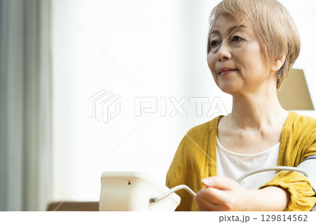 リビングで血圧を測定するシニア女性 リビングで血圧を測定するシニア女性 129814562