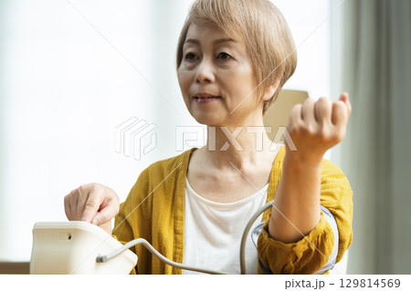 リビングで血圧を測定するシニア女性 リビングで血圧を測定するシニア女性 129814569