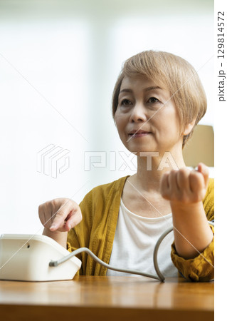 リビングで血圧を測定するシニア女性 リビングで血圧を測定するシニア女性 129814572