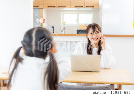 リビングで勉強をする小学生の女の子とテレワークのママ 129814683