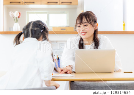 リビングで勉強をする小学生の女の子とテレワークのママ 129814684