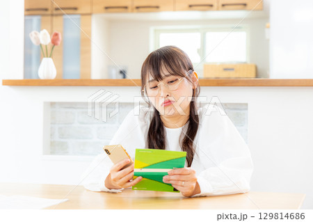 スマホと通帳を見る女性 129814686