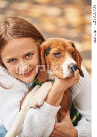 Sitting, holding animal and looking into the camera. Young woman is with her dog in the park Sitting, holding animal and looking into the camera. Young woman is with her dog in the park 129816735