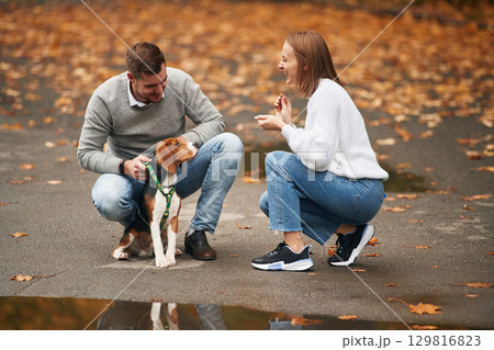 Sitting, playing with animal. Lovely couple are with their cute dog outdoors Sitting, playing with animal. Lovely couple are with their cute dog outdoors 129816823