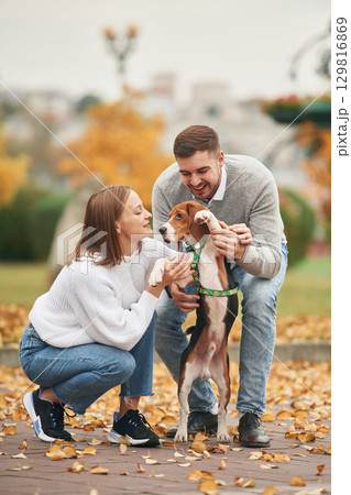 Holding animal by the legs, making him stand straight. Lovely couple are with their cute dog outdoors Holding animal by the legs, making him stand straight. Lovely couple are with their cute dog outdoors 129816869
