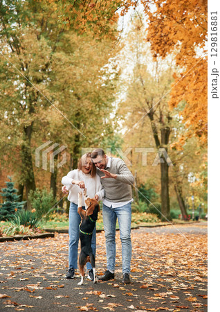 Fallen leaves are on the ground. Lovely couple are with their cute dog outdoors 129816881