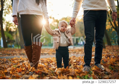 Little boy is holding hands of the parents. Standing in the autumn park Little boy is holding hands of the parents. Standing in the autumn park 129817257