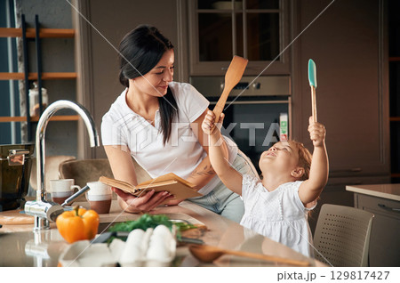 Mother with her daughter are preparing food on the kitchen Mother with her daughter are preparing food on the kitchen 129817427