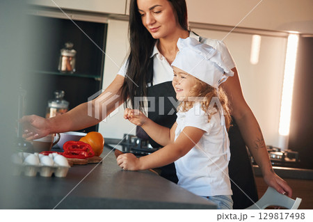 Side view. Mother with her daughter are preparing food on the kitchen Side view. Mother with her daughter are preparing food on the kitchen 129817498