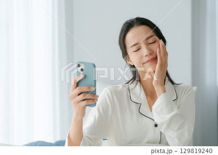 スマホを持つ寝起きの女性 129819240